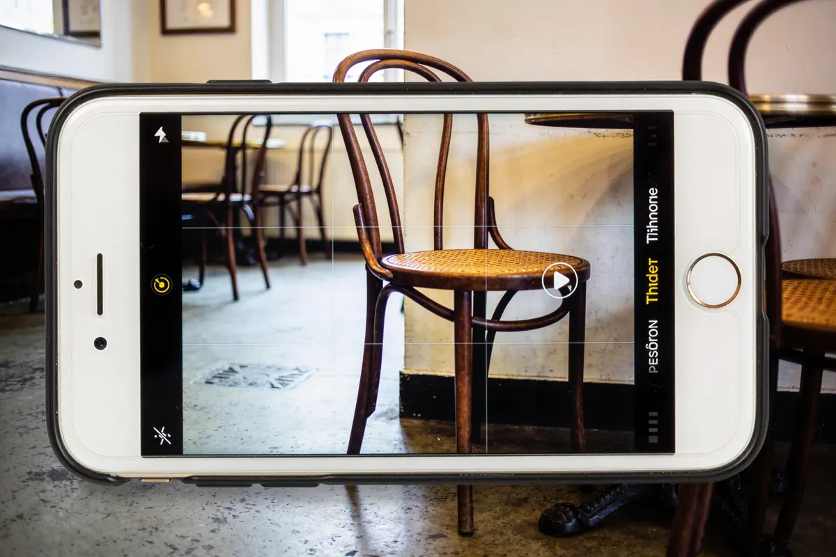 Photo de chaise en bois capturée depuis un smartphone, café en arrière-plan avec tables et chaises assorties.